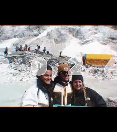 Three people smiling at the camera in a snowy mountain environment with other people and structures in the background.