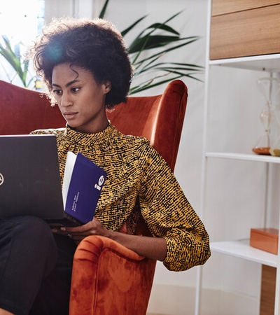 A person sitting in an orange armchair, using a laptop while focused on the screen.