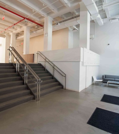 A modern interior space featuring a staircase with grey steps, white walls, and exposed red ceiling pipes.