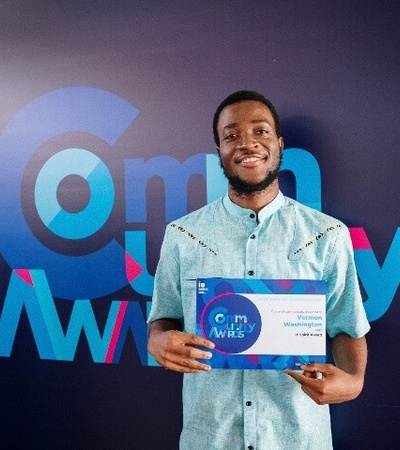 A man smiling and holding an award certificate in front of a banner with 'IE University' and 'Com AWARDS' logos.