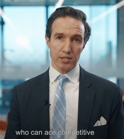 A man in a business suit is speaking in a modern office environment.