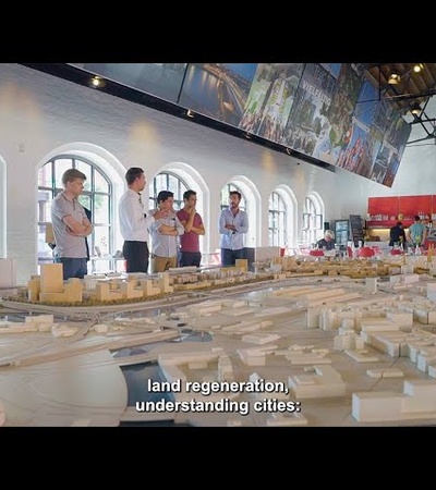 A group of people standing around a large architectural model inside a well-lit room.