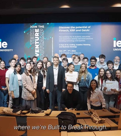 A group of students and a few adults gather in a university lecture hall under a promotional banner.