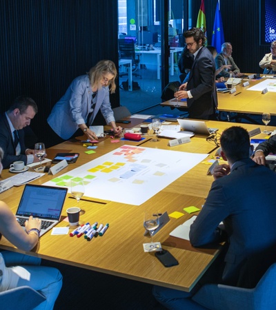 A collaborative meeting in a modern conference room with people discussing and working on a large table covered in notes and materials.