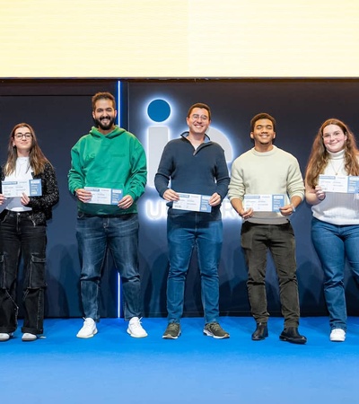 A group of six people smiling and holding certificates, standing with a flight attendant in a corporate environment.