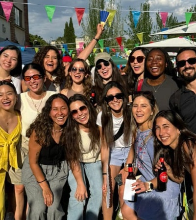 A group of joyful people posing together at an outdoor festival with colorful flags and a sunny sky.