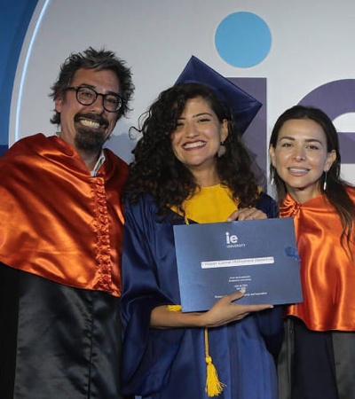 Three people in graduation attire, one holding a diploma, celebrating at a graduation ceremony.