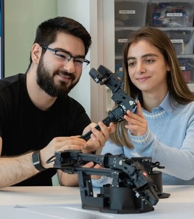Two people are collaborating on a robotics project, focusing on a robotic arm.