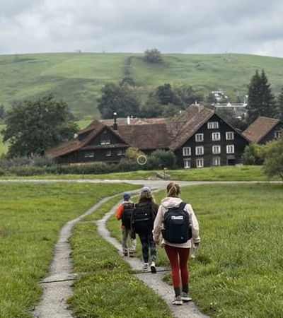 A group of hikers walking along a path in a green countryside with a house in the background.