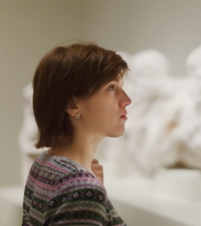 A woman gazes thoughtfully at a group of white marble sculptures in a gallery.