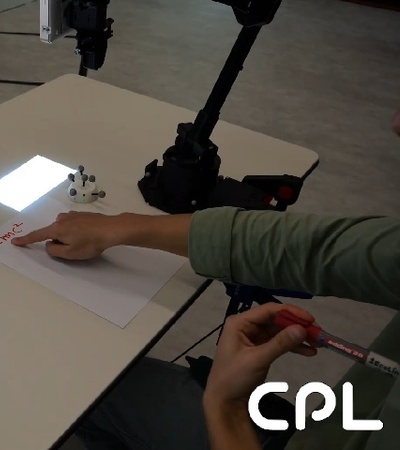 A person is writing on a piece of paper while interacting with a computer showing the Google homepage.