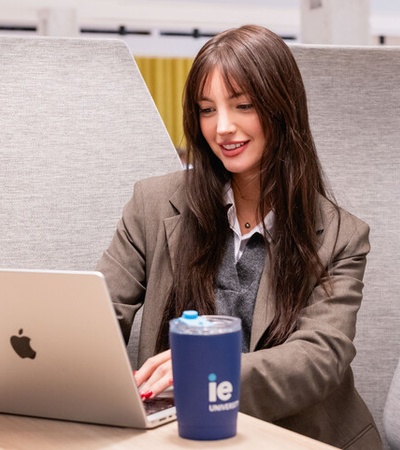 A young woman is working on her laptop while smiling at a modern workspace.
