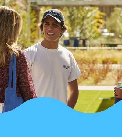 Three young adults talking and smiling outdoors on a sunny day.