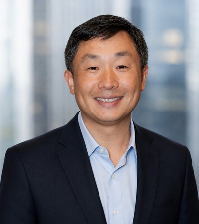 A smiling man in a business suit with a blurred cityscape in the background.