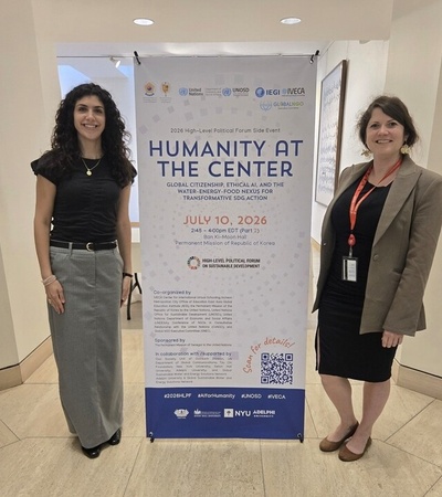 Two women stand beside a poster announcing an event titled 'Humanity at the Center'.