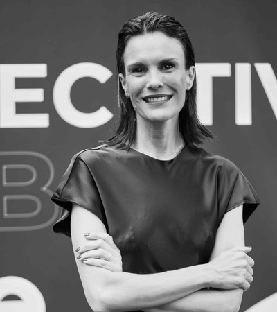 Black and white image of a smiling woman with arms crossed, standing in front of a sign that includes the word 'EXECUTIVE'.