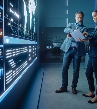 Two colleagues are discussing data on a digital display in a modern office environment.