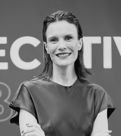 Black and white image of a smiling woman with crossed arms wearing a simple blouse, standing in front of a blurred background with the words 'ECTIVA 3'.