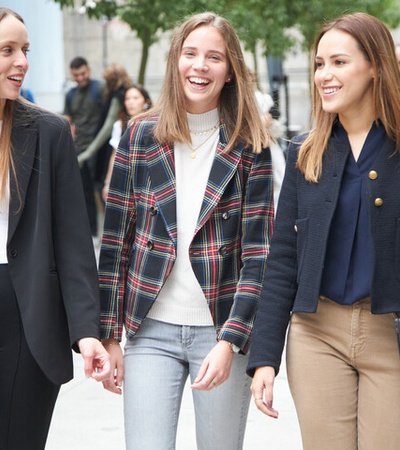 Three women are walking together casually, smiling on a city street.