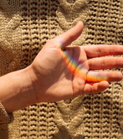 A hand displaying a rainbow reflection against a knitted fabric background.