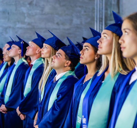 A group of graduates wearing blue caps and gowns, looking upward during a ceremony.