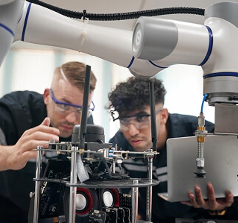 Two individuals are closely examining a robotic arm and its components in a laboratory setting.