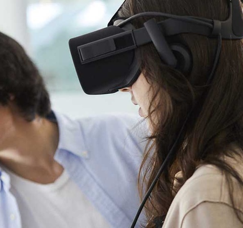 A woman uses VR headset with a man observing nearby in a modern indoor setting.