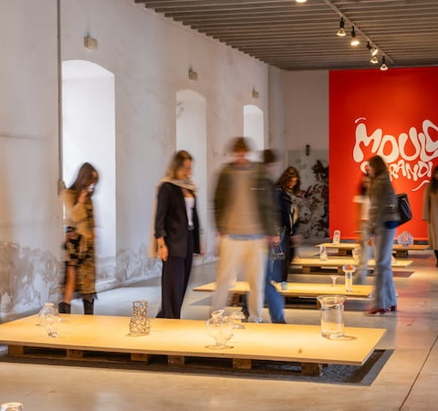 People viewing an art exhibition in a gallery with red and white walls and modern artwork installations.