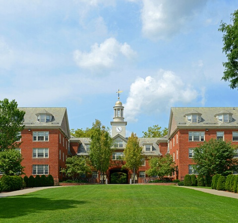 A scenic view of a college campus featuring brick buildings and a clock tower surrounded by greenery.