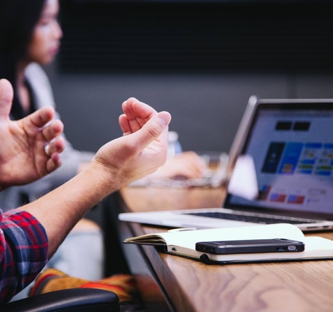 Computer in a table, hand os a person explaining information in a meeting.