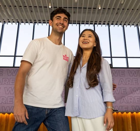 Two young adults are smiling together in a modern indoor setting with illuminated displays.