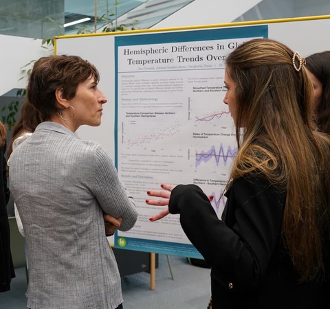 Two women are discussing in front of a scientific poster about temperature trends.