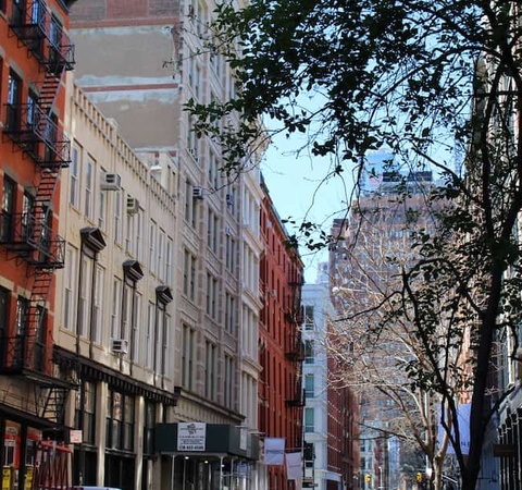 A quiet street in a city with historic buildings and a glimpse of a tall modern skyscraper in the distance.