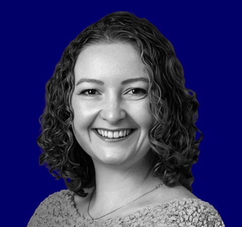 A grayscale image of a smiling woman with curly hair against a solid blue background.