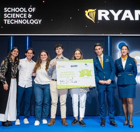 A group of young people proudly holding a large check on stage, flanked by flight attendants, at a Ryanair event.