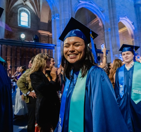 A joyful graduate wearing a blue cap and gown smiling at a ceremony.