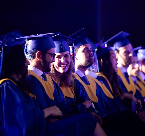 A group of graduates in caps and gowns sitting in a ceremony.