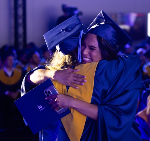 Two graduates embrace joyfully during a graduation ceremony.