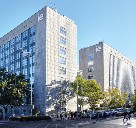 A modern university campus with glass buildings and trees in a clear blue sky.