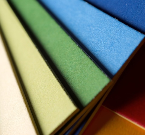 A close-up of colorful paper sheets aligned in a row, showcasing a gradient of colors from red to blue.