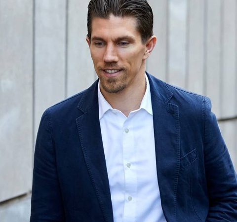 A man in a professional blue suit and white shirt walks confidently in an urban setting.