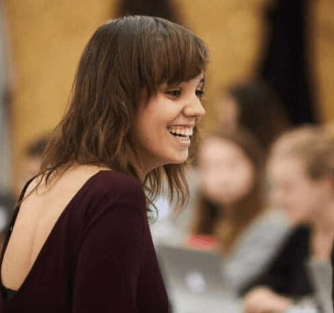 A young woman with a joyful expression is looking to the side in a crowded room.