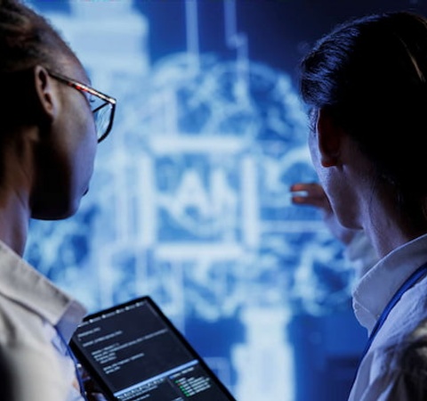 Two individuals are analyzing data on a large display while using a tablet.