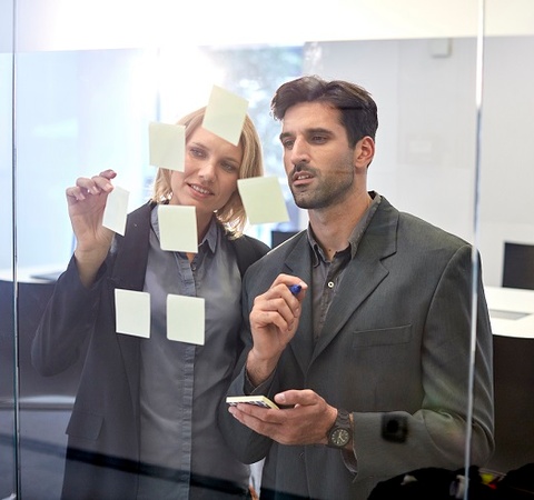 Men and woman sticking post-it in a transparent white  board