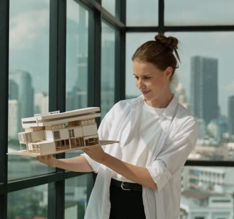 A woman is holding a architectural model of a building in a modern urban setting.