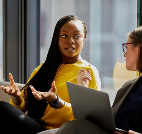 Two women engaged in a conversation in a modern office setting.