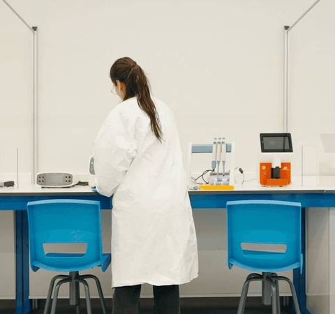 A woman in a white lab coat stands at a workstation in a clean and organized laboratory.