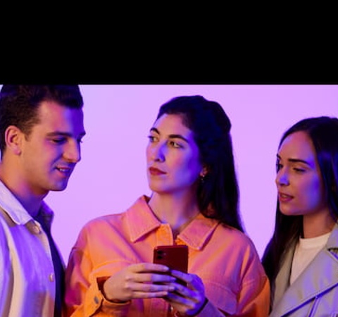 Three young adults looking at a smartphone with a colorful lighting background.