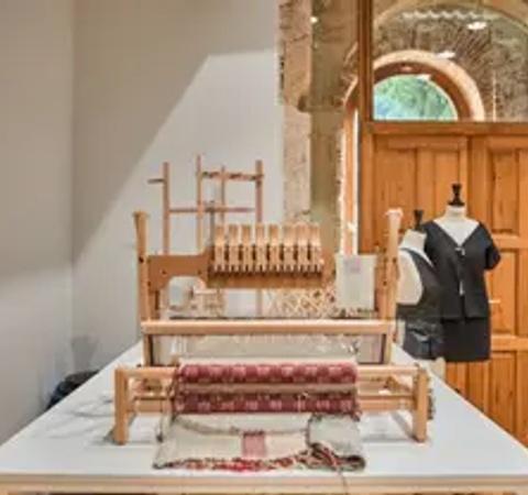 A traditional weaving loom and a mannequin next to a wooden door in a room with rustic stone architecture.