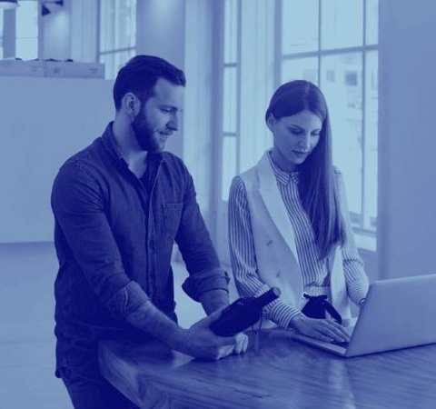 A man and a woman examining a product with a laptop on a wooden table in an office environment.